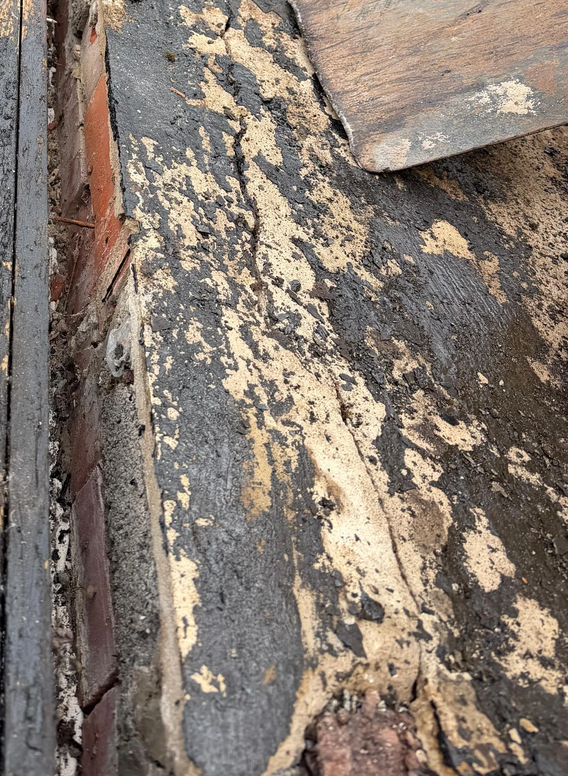 Old roof-covering remnants beside a brick roof edge, with a timber board at the top