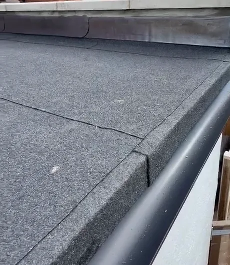 Mineral-finished flat-roof felt with seams, an edge gutter and flashing beneath coping stones