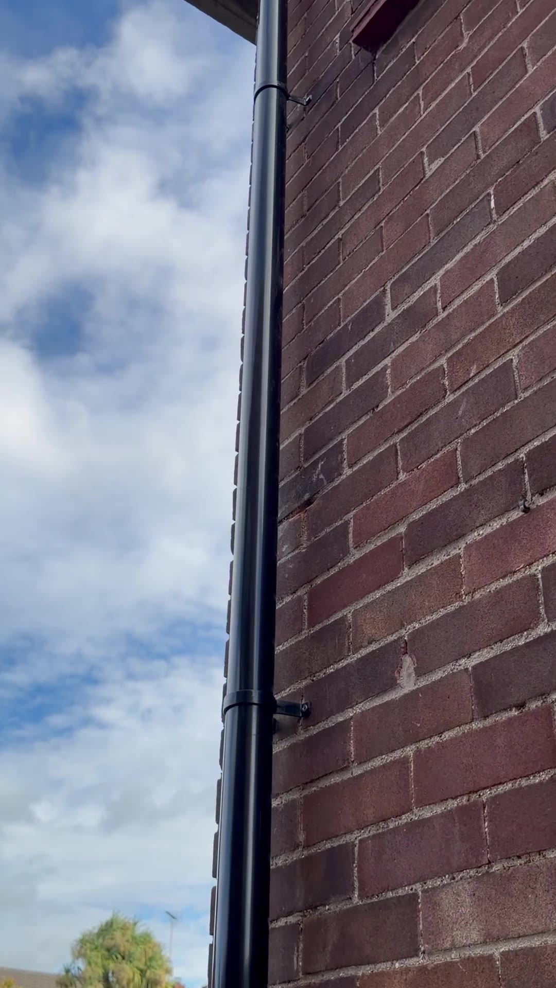 Aligned black round uPVC downpipe secured with new brackets on brickwork