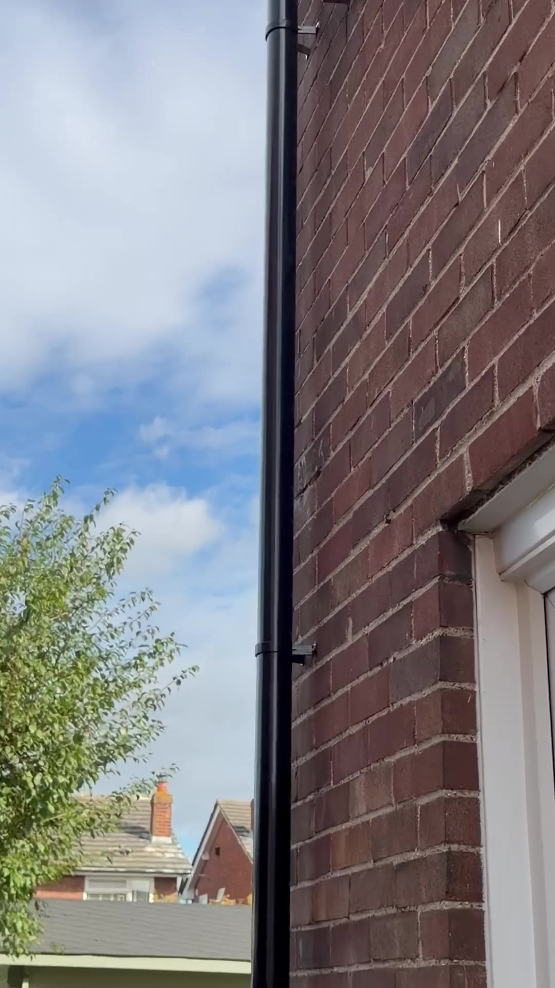 Black round uPVC downpipe with new brackets beside a brick wall and window