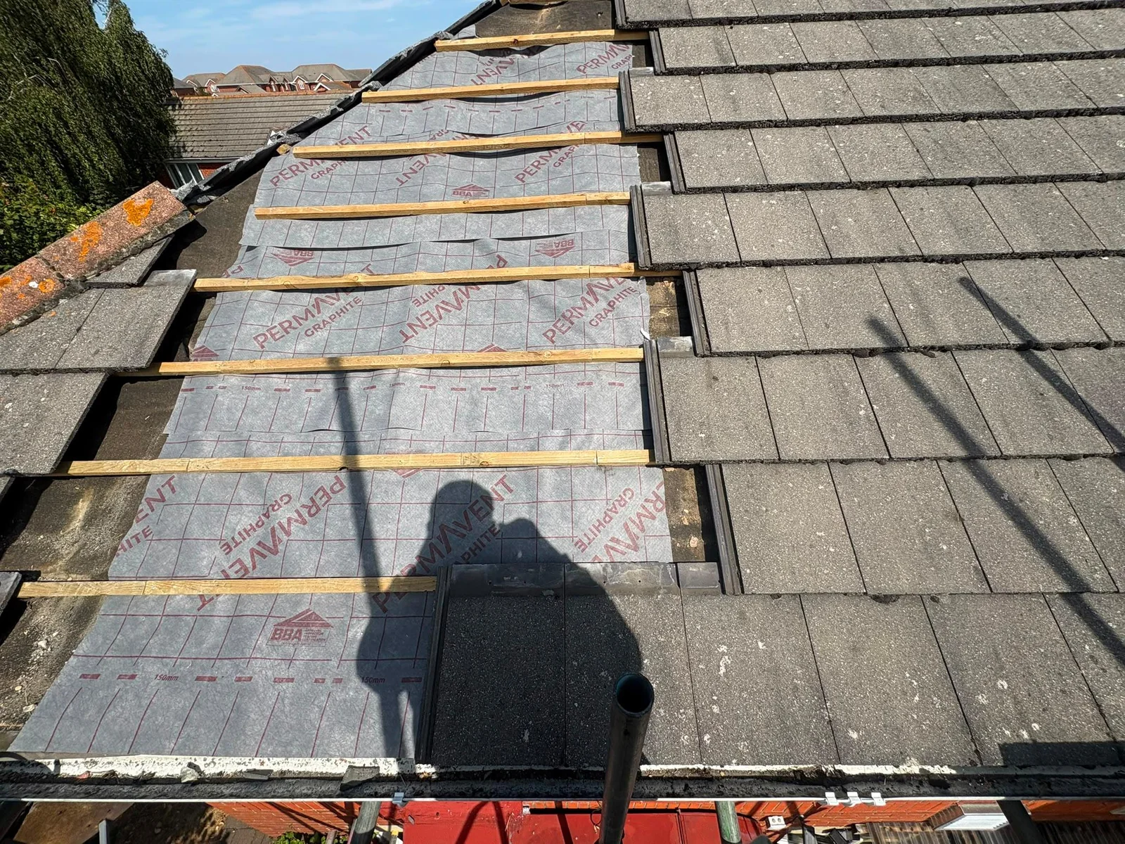 Roofing membrane and timber battens beside existing grey roof tiles