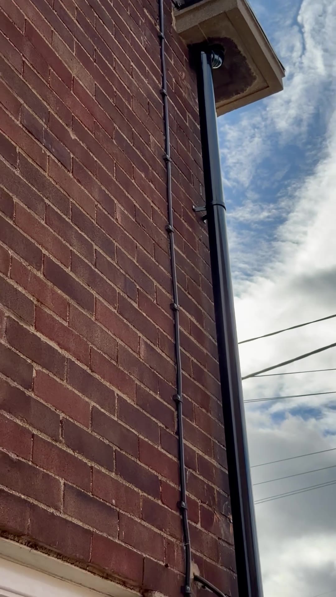 Replacement black round uPVC downpipe running from the eaves along a brick wall